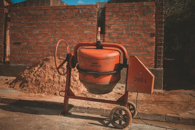 Orange concrete mixer with sand pile at a UK construction site for mixing concrete