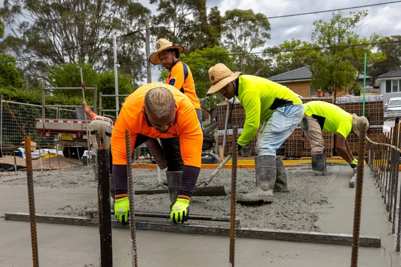 Construction workers pouring and levelling wet concrete on a reinforced slab